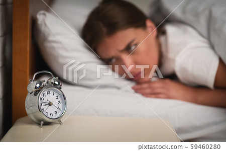 Young Woman Looking At Clock Lying In Bed At Home Young Woman Looking At Clock Lying In Bed At Home 59460280