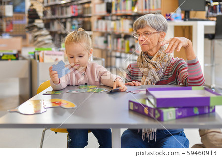 Granddaughter and grandmother put together a puzzle in the city library 59460913