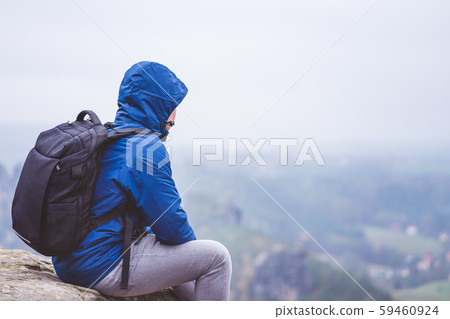Lonely hiker wear outdoor clothing with backpack sitting on mountain edge, enjoying view of 59460924