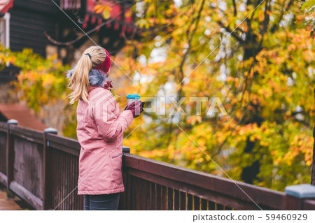 Adult blond woman holds a cup of herbal tee in hands on wooden bridge with beautiful golden autumn Adult blond woman holds a cup of herbal tee in hands on wooden bridge with beautiful golden autumn 59460929