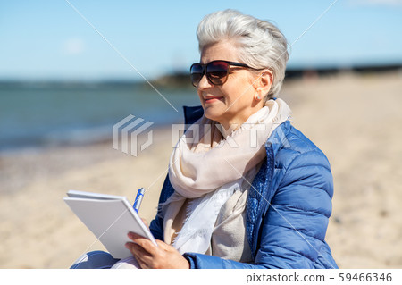 senior woman writing to notebook on summer beach senior woman writing to notebook on summer beach 59466346