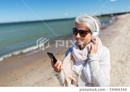 old woman in headphones with smartphone on beach old woman in headphones with smartphone on beach 59466348