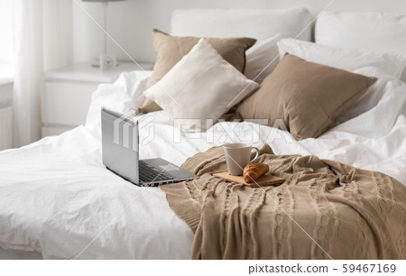laptop, cup of coffee and croissant on bed at home 59467169