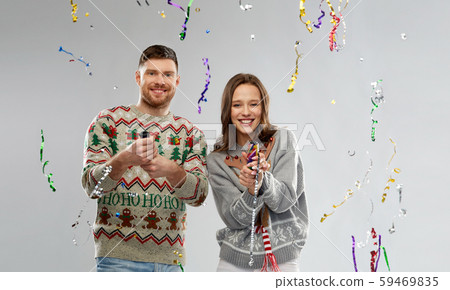 couple in christmas sweaters popping party poppers 59469835