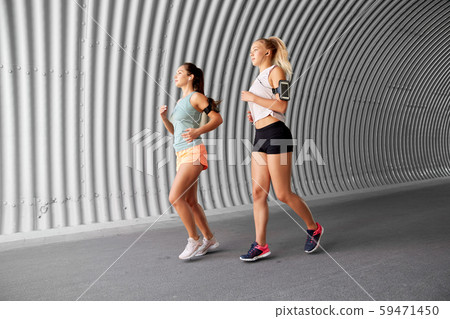 young women with earphones and smartphones running young women with earphones and smartphones running 59471450