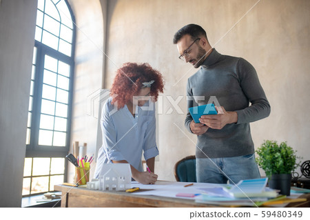 Bearded interior designer watching trainee making sketches 59480349