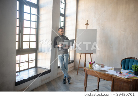 Interior designer holding laptop while standing near window Interior designer holding laptop while standing near window 59480701