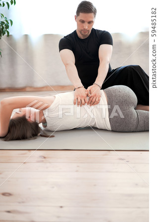 Sportswoman in sportswear stretching on rug with male trainer in gym 59485182