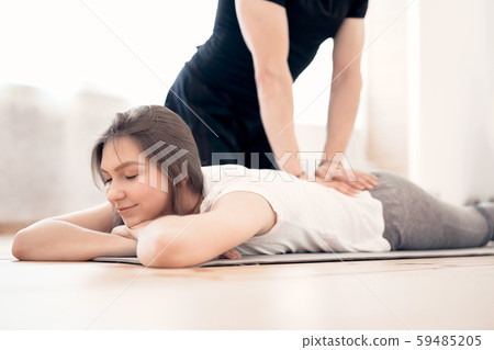 Woman doing stretching on grey mat with male trainer in gym 59485205