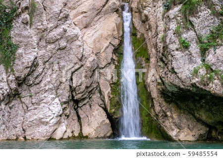 A high waterfall falls from a cliff into a clear lake A high waterfall falls from a cliff into a clear lake 59485554