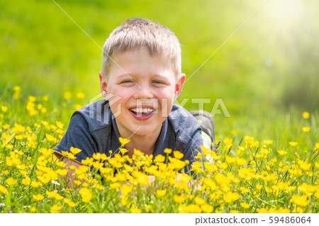 A boy with a smile is resting on a green lawn with yellow wildflowers A boy with a smile is resting on a green lawn with yellow wildflowers 59486064