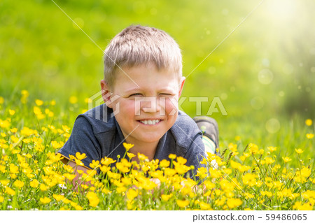A boy with a smile is resting on a green lawn with yellow wildflowers A boy with a smile is resting on a green lawn with yellow wildflowers 59486065