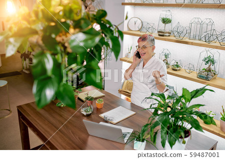 Top view on mature woman florist talking on phone standing around plants 59487001