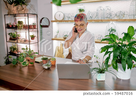 Mature caucasian florist wearing eyeglasses in workplace talking on mobile phone 59487016