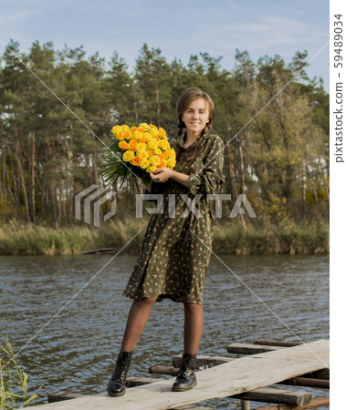 Beautiful girl with a bouquet of yellow roses. Effective woman near the river. Pretty Woman. Teen girl with yellow roses. Girl on the old bridge. 59489034