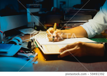 Businessman writing on document while working late in office. Businessman writing on document while working late in office. 59491392