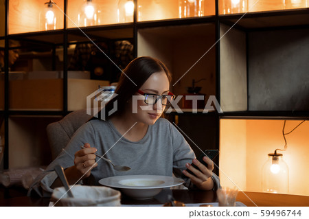 Woman eating soup and browsing smartphone in cafe Woman eating soup and browsing smartphone in cafe 59496744
