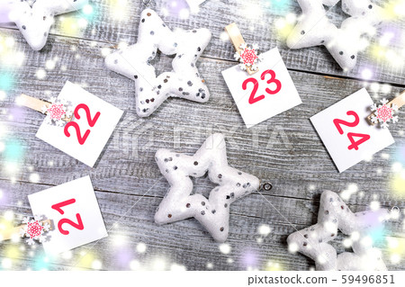 Close-up 21-24 part of Advent calendar with sheets with numbers on decorative clips, white christmas toys stars, colored blurred lights on white wooden snowy background. Christmas festive decorations. 59496851