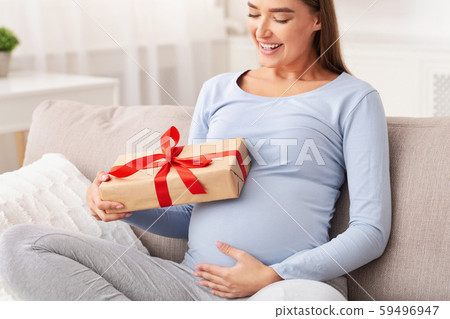Pregnant Woman Holding Wrapped Gift Box Smiling Sitting On Sofa 59496947