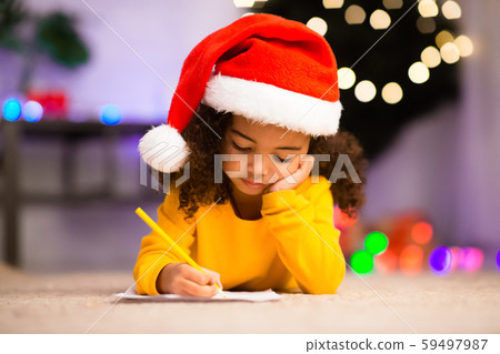 Pretty girl in Santa hat writes letter to Santa near christmas tree Pretty girl in Santa hat writes letter to Santa near christmas tree 59497987