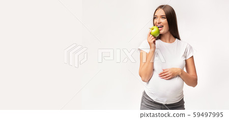 Expectant Woman Eating Apple Touching Belly Standing In Studio, Panorama Expectant Woman Eating Apple Touching Belly Standing In Studio, Panorama 59497995