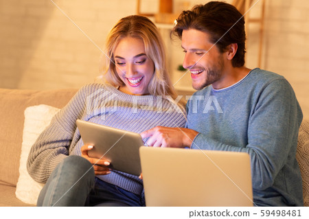Couple Using Laptop And Tablet Websurfing Sitting On Sofa Indoor Couple Using Laptop And Tablet Websurfing Sitting On Sofa Indoor 59498481