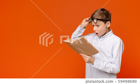 Emotional teenager reading exciting book, raising his glasses in amazement 59498690