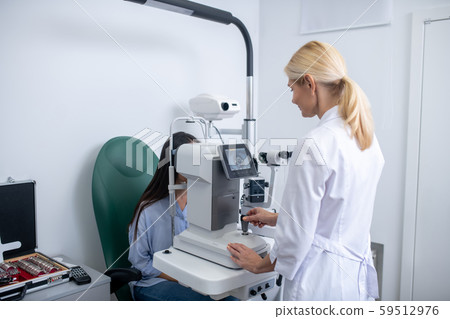 Eye doctor standing near modern equipment and examining woman Eye doctor standing near modern equipment and examining woman 59512976