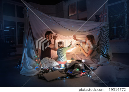 Family sitting in a teepee, reading stories with the flashlight 59514772
