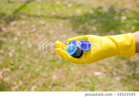 Hand with yellow glove hold lot of bottle caps in park or garden Hand with yellow glove hold lot of bottle caps in park or garden 59523595