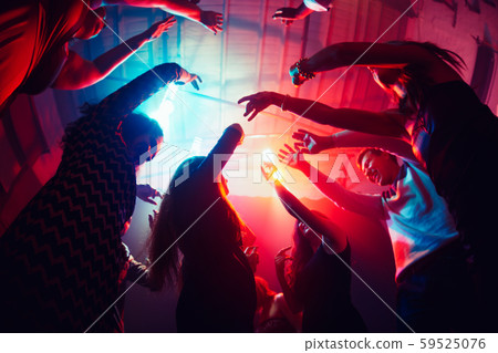 A crowd of people in silhouette raises their hands against colorful neon light on party background 59525076