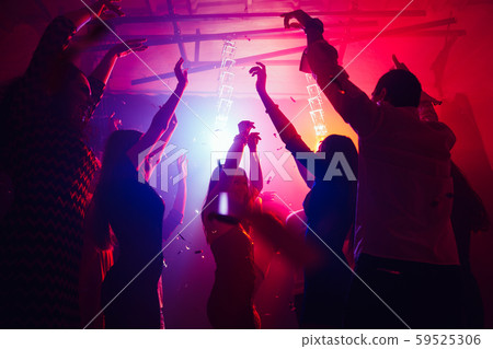 A crowd of people in silhouette raises their hands against colorful neon light on party background 59525306