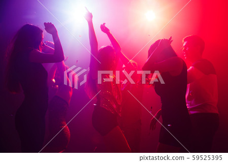 A crowd of people in silhouette raises their hands against colorful neon light on party background A crowd of people in silhouette raises their hands against colorful neon light on party background 59525395