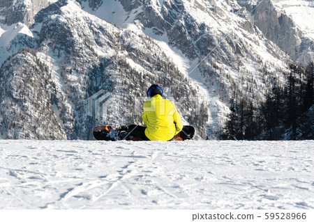A snowboarder in a yellow jacket sits on a ski 59528966
