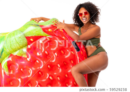 Pretty african female stands in swimsuit with rubber beach strawberry mattress and smiles isolated Pretty african female stands in swimsuit with rubber beach strawberry mattress and smiles isolated 59529238