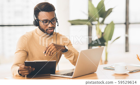 Concentrated consultant with headset looking at laptop Concentrated consultant with headset looking at laptop 59529614