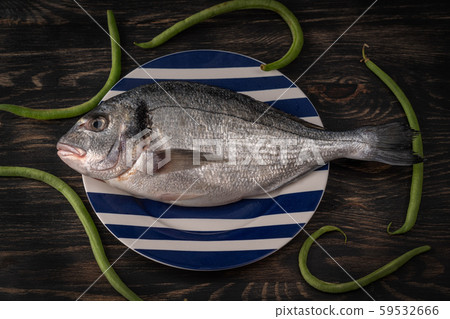 Fish Sparus aurata on a plate with asparagus beans, on a wooden background. Fish Sparus aurata on a plate with asparagus beans, on a wooden background. 59532666