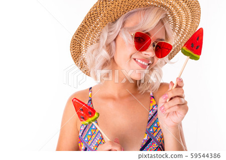 Happy blonde caucasian female stands in swimsuit with watermelon lolipops and smiles isolated on Happy blonde caucasian female stands in swimsuit with watermelon lolipops and smiles isolated on 59544386