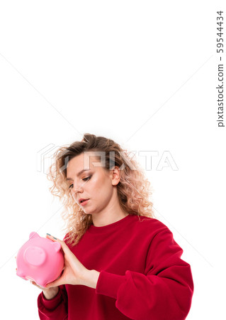 Caucasian girl with curly fair hair trying to get money from the pink pig moneybox, portrait 59544434
