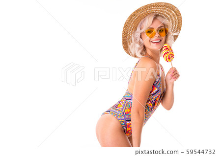 Pretty blonde caucasian female stands in swimsuit with lolipop and smiles isolated on white Pretty blonde caucasian female stands in swimsuit with lolipop and smiles isolated on white 59544732