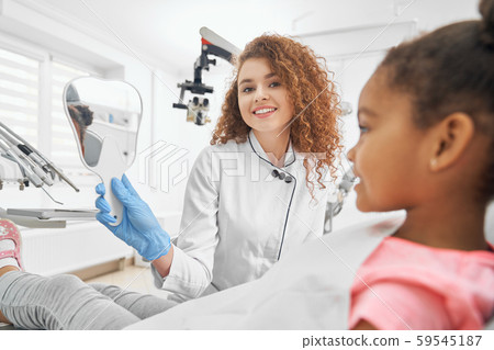 Dentist holding mirror in form of tooth for girl. Dentist holding mirror in form of tooth for girl. 59545187