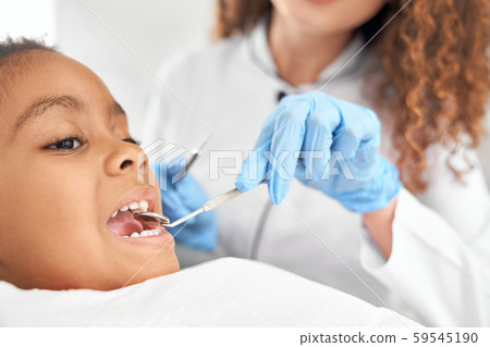Dentist looking at teeth of girl with dental mirror. 59545190