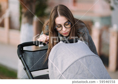 Beautiful mom look in to the stroller. Young mother walking with baby. Happy family Beautiful mom look in to the stroller. Young mother walking with baby. Happy family 59546558