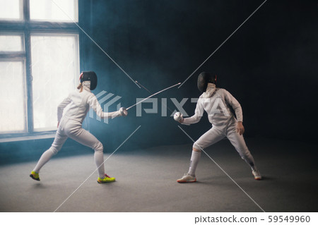 A fencing training - two women in protective costumes having a duel 59549960