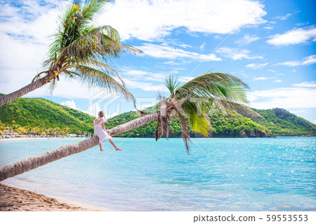 Adorable little girl sitting on palm tree during summer vacation on white beach 59553553