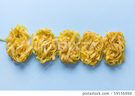 Raw egg pasta shape reginella rolled up by portion on blue. View from above. Raw egg pasta shape reginella rolled up by portion on blue. View from above. 59556998