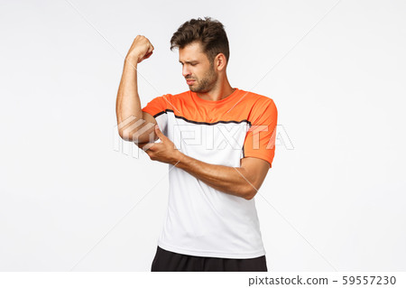 Upset gloomy handsome young man feeling weak as raising arm, touching his muscle and frowning sad Upset gloomy handsome young man feeling weak as raising arm, touching his muscle and frowning sad 59557230