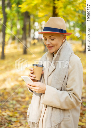 Mature pleased woman using a gadget outdoors Mature pleased woman using a gadget outdoors 59560727