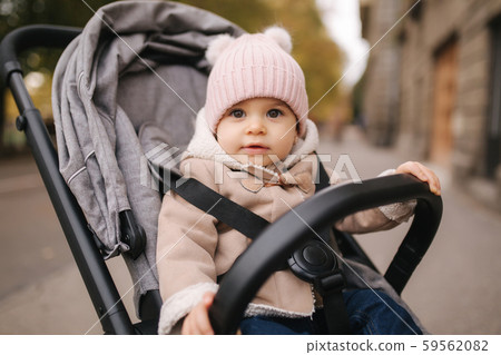 Cute little baby in pram. Adorable baby girl in autumn sitting in her pram Cute little baby in pram. Adorable baby girl in autumn sitting in her pram 59562082