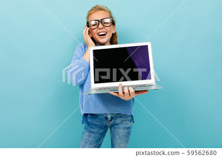 surprised excited schoolgirl laughs against a blue wall with a laptop, holds her hand to her head surprised excited schoolgirl laughs against a blue wall with a laptop, holds her hand to her head 59562680